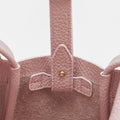 Close-up of a pink pebbled leather Mini Song Bag interior, showing the strap attachment with gold hardware and suede lining.