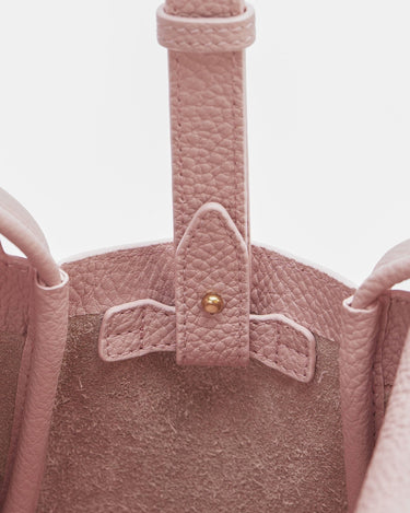 Close-up of a pink pebbled leather Mini Song Bag interior, showing the strap attachment with gold hardware and suede lining.