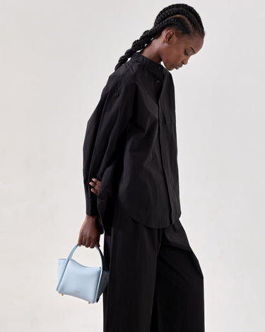 Mini Song Bag in Sky blue pebbled leather, held by a woman in a black outfit.