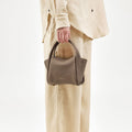 Taupe pebble-grained leather Mini Song Bag held by a person in beige linen attire
