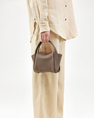Taupe pebble-grained leather Mini Song Bag held by a person in beige linen attire