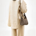 Taupe Mini Song Bag in textured leather with gold hardware, worn by a woman in a matching linen outfit.