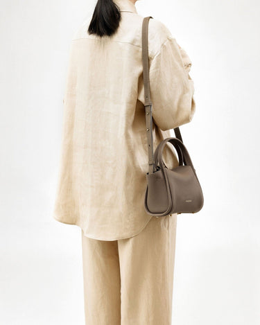 Taupe Mini Song Bag in textured leather with gold hardware, worn by a woman in a matching linen outfit.