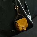 Ochre suede Mini Yore AirPods Case with snap closure, attached to a black leather Songmont handbag.
