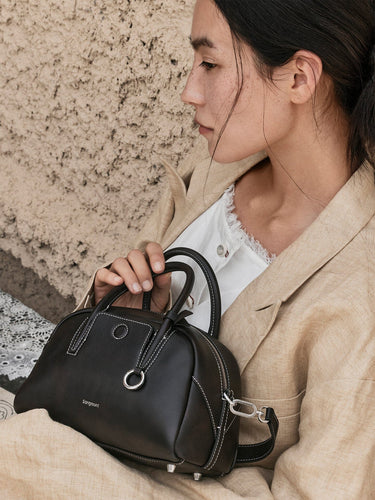Woman holding black Mini Yore Bowling Bag by Songmont, made of full-grain leather with white stitching.