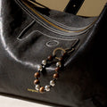 Black leather handbag featuring a sandalwood and silver bead charm attached to the side, with embossed "Songmont" logo.