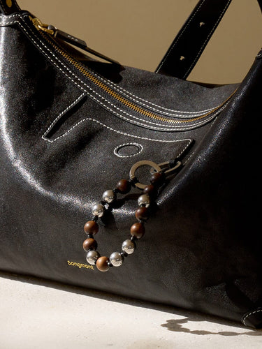 Black leather handbag featuring a sandalwood and silver bead charm attached to the side, with embossed "Songmont" logo.