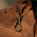 Topaz peace beads charm with golden and brown beads on a brown suede bag.