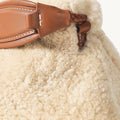 Amber shearling clutch with braided leather strap detail, showcasing cozy texture and stitching.