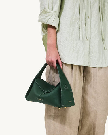 Small dark green pebbled leather drippy roof bag with white stitching and gold hardware, held by a person.