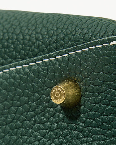 Green full-grain leather bag detail with stitched seam and 'song mont' engraved brass hardware.