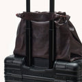 Dark brown leather Small Gather Bag Set draped over the handle of a black suitcase.