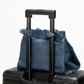 Small Gather Bag Set in navy blue leather, a versatile tote for travel, secured on a suitcase handle.