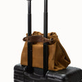 Ochre suede Small Gather Bag Set resting on a black rolling suitcase, featuring leather straps and travel-ready design.