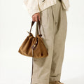 Ochre suede small gather bag set with adjustable straps, held by a person in a cream distressed cardigan and linen pants.