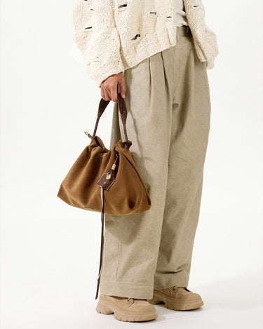 Ochre suede small gather bag set with adjustable straps, held by a person in a cream distressed cardigan and linen pants.