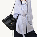 Black leather small gather bag set with gold charm, worn by a person in a pinstripe shirt.