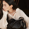 Woman holding a black leather Small Gather Bag Set with drawstring closure and braided straps. Elegant and stylish accessory.