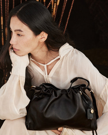Woman holding a black leather Small Gather Bag Set with drawstring closure and braided straps. Elegant and stylish accessory.