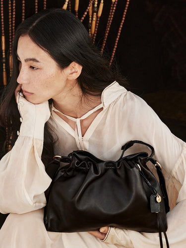 Woman holding a black leather Small Gather Bag Set with drawstring closure and braided straps. Elegant and stylish accessory.