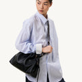 Black leather Small Gather Bag Set with drawstring closure, worn by a model in a blue pinstripe shirt.