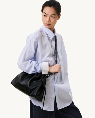 Black leather Small Gather Bag Set with drawstring closure, worn by a model in a blue pinstripe shirt.