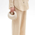 Small Luna Bag in ivory pebble-grain leather with gold hardware, worn by a person in cream linen attire.