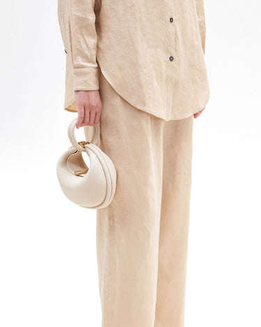 Small Luna Bag in ivory pebbled leather, held by hand with a looped handle and gold hardware.