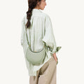 Small Luna Bag in jade green, crafted from full-grain leather with gold hardware, worn on the shoulder by a woman.