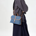 Small Shan Satchel Bag in denim with tan leather trim and gold buckle.