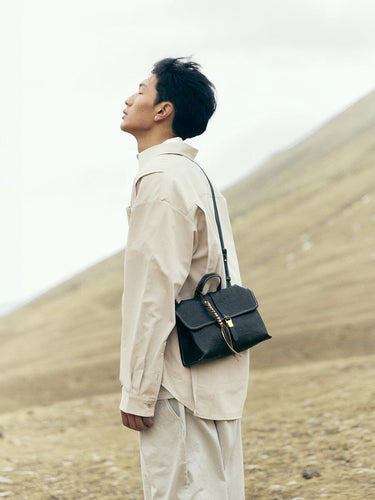 Onyx Small Shan Satchel Bag with leather tassel and gold hardware, worn crossbody outdoors.