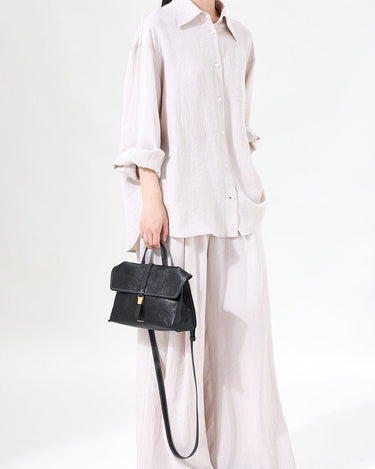 Black Small Shan Satchel Bag with textured leather and gold hardware, worn by a model in linen clothing.
