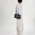 Small Shan Satchel Bag in Onyx: Textured vegetable-tanned leather, gold clasp, top handle, and adjustable strap.
