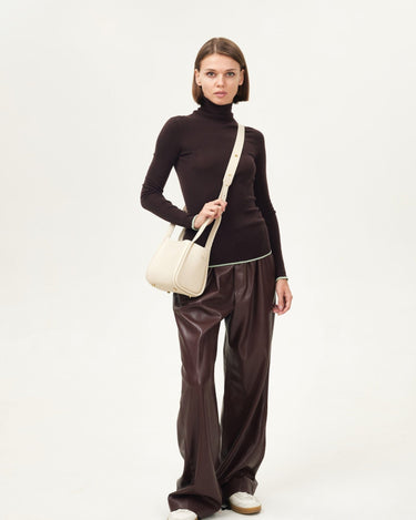 Small Song Bag in cream full-grain leather with magnetic closure, worn by a model.