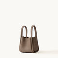 Small Song Bag in taupe pebbled full-grain leather, minimalist bucket design with dual top handles.