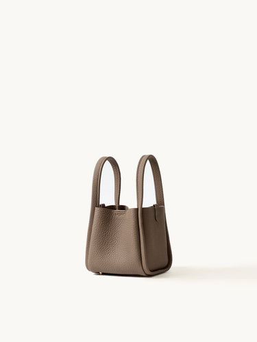 Small Song Bag in taupe pebbled full-grain leather, minimalist bucket design with dual top handles.