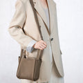 Taupe full-grain leather Small Song Bag worn by a woman in a cream blazer.