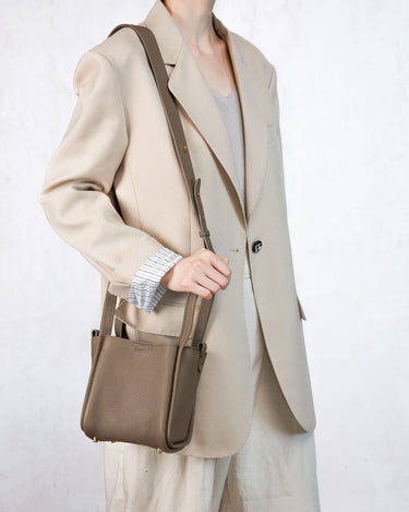 Taupe full-grain leather Small Song Bag worn by a woman in a cream blazer.