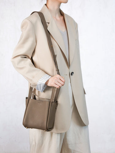 Taupe full-grain leather Small Song Bag worn by a woman in a cream blazer.