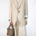Small Song Bag in taupe pebbled leather, styled with a beige blazer and pants.