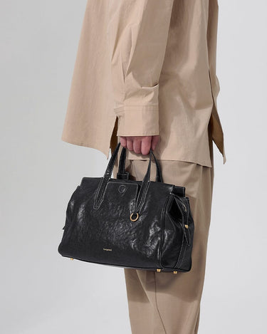Small Yore Duffle Bag in onyx black vegetable-tanned leather with white stitching and gold hardware, held by a person.