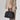 Small Yore Duffle Bag in onyx black vegetable-tanned leather with white stitching and gold hardware, held by a person.