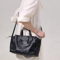 Small Yore Duffle Bag in Onyx: Vegetable-tanned leather travel bag with white stitching and gold hardware, worn by a woman.