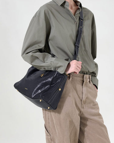 Small Yore Duffle Bag in Onyx, made from vegetable-tanned leather with gold hardware and white stitching, worn by a model.