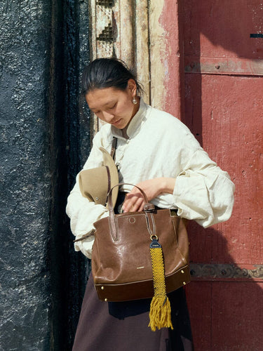 Small Yore Duffle Bag in Sandal brown leather with yellow tassel, carried by a woman.