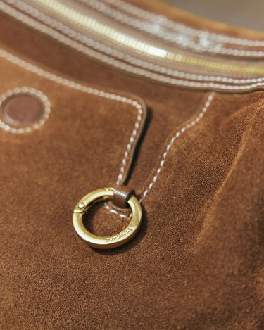 Close-up of Sandal Suede Small Yore Hobo Bag featuring a brass ring detail with embossed "Songmont" logo.