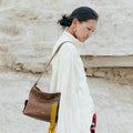 Small Yore Hobo Bag in Sandal brown leather with yellow tassel charm, worn by a woman.