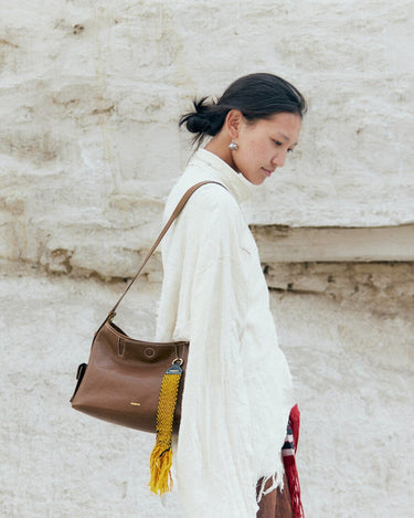 Small Yore Hobo Bag in Sandal brown leather with yellow tassel charm, worn by a woman.