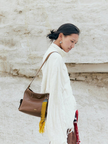Small Yore Hobo Bag in Sandal brown leather with yellow tassel charm, worn by a woman.