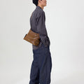 Small Yore Hobo Bag in Sandal color, crafted from vegetable-tanned leather with adjustable strap, worn by a man.